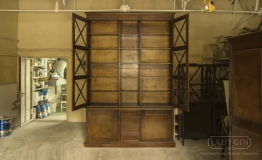 Внутренняя покраска высокого деревянного книжного шкафа в стиле прованс со стеклянными дверками на цоколе фото