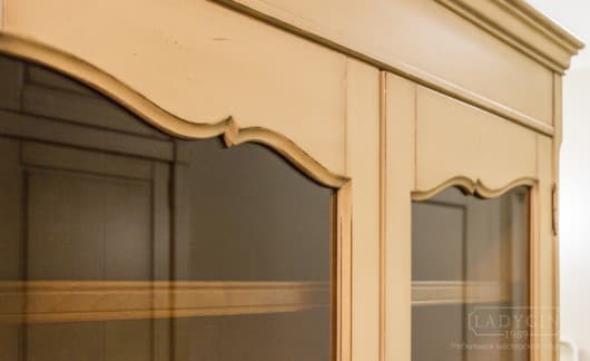 Резные элементы на стеклянных дверках белой деревянной витрины на цоколе в классическом французском стиле фото
