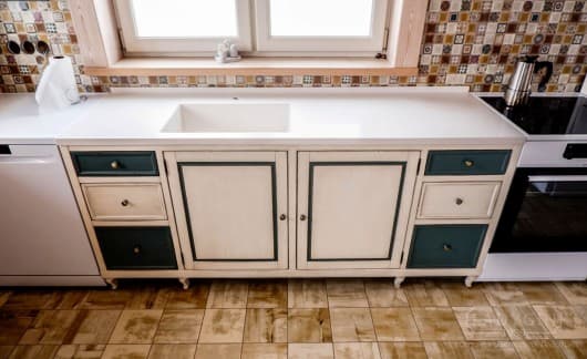 Белая деревянная кухня во французском стиле со столешницей из искусственного камня и отлитой раковиной и зелёными ящиками фото