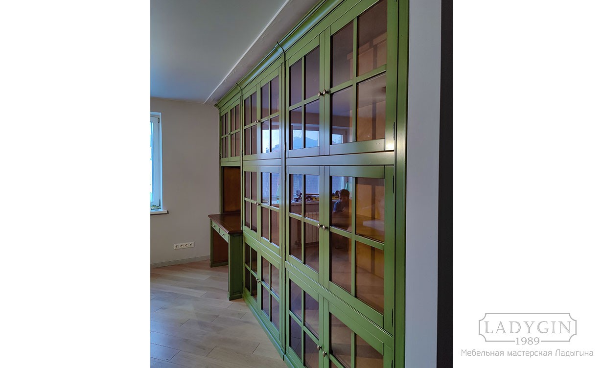 Стеклянные дверки зеленой закрытой библиотеки из дерева в классическом стиле с рабочим местом фото